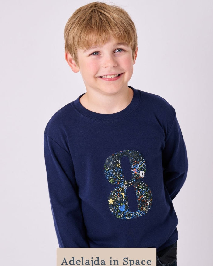 A smiling boy wearing a navy cotton t-shirt with the number 8 on the front cut from space liberty print
