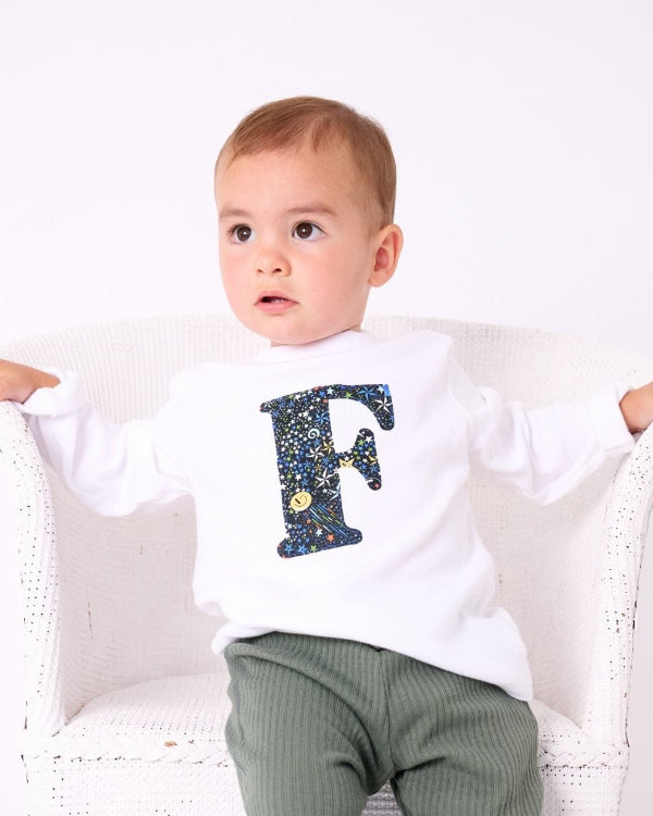 a 1 year old boy wearing a personalised kids whitet-shirt with an initial cut from adelajda in space liberty print on the front