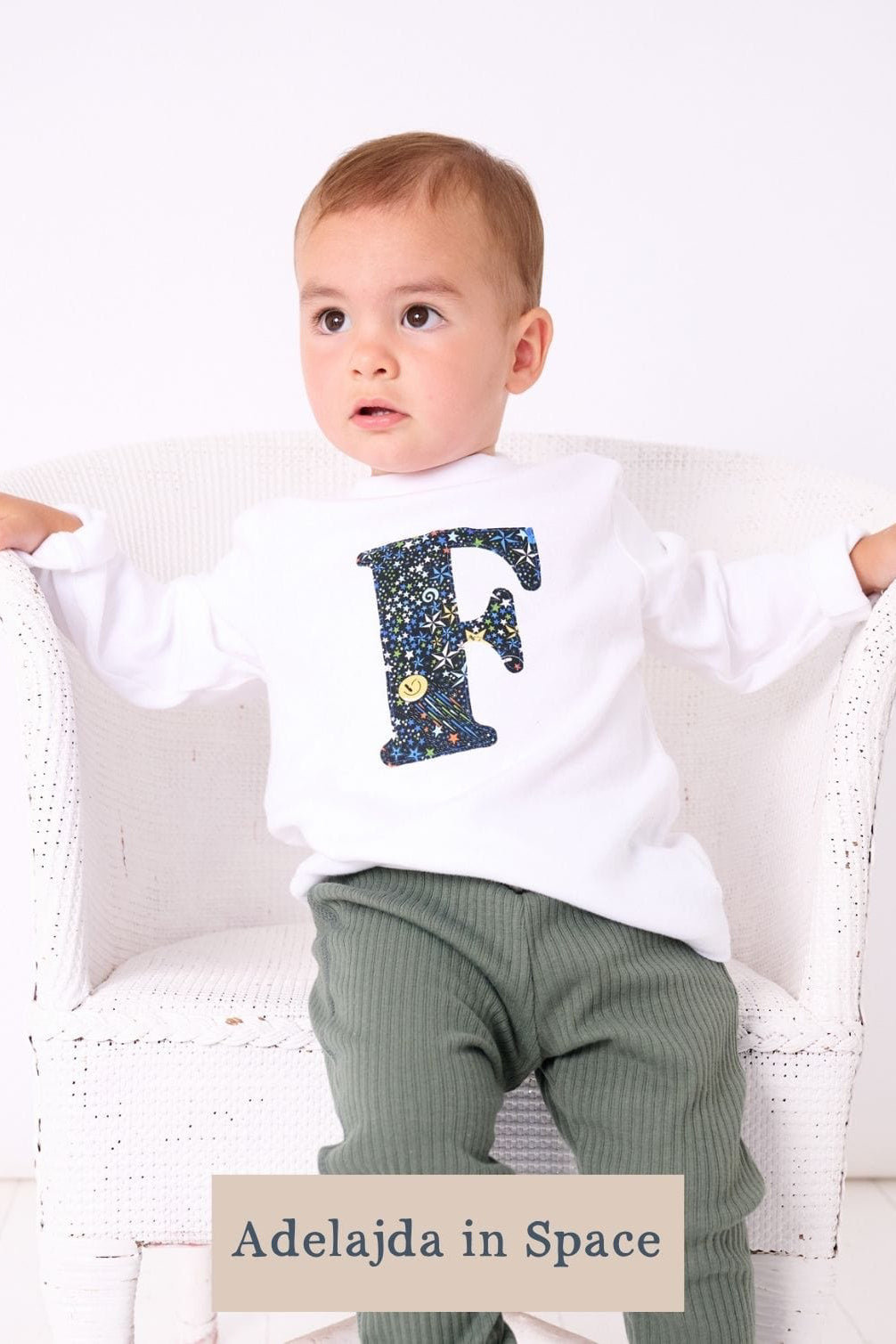 a 1 year old boy wearing a personalised kids whitet-shirt with an initial cut from adelajda in space liberty print on the front