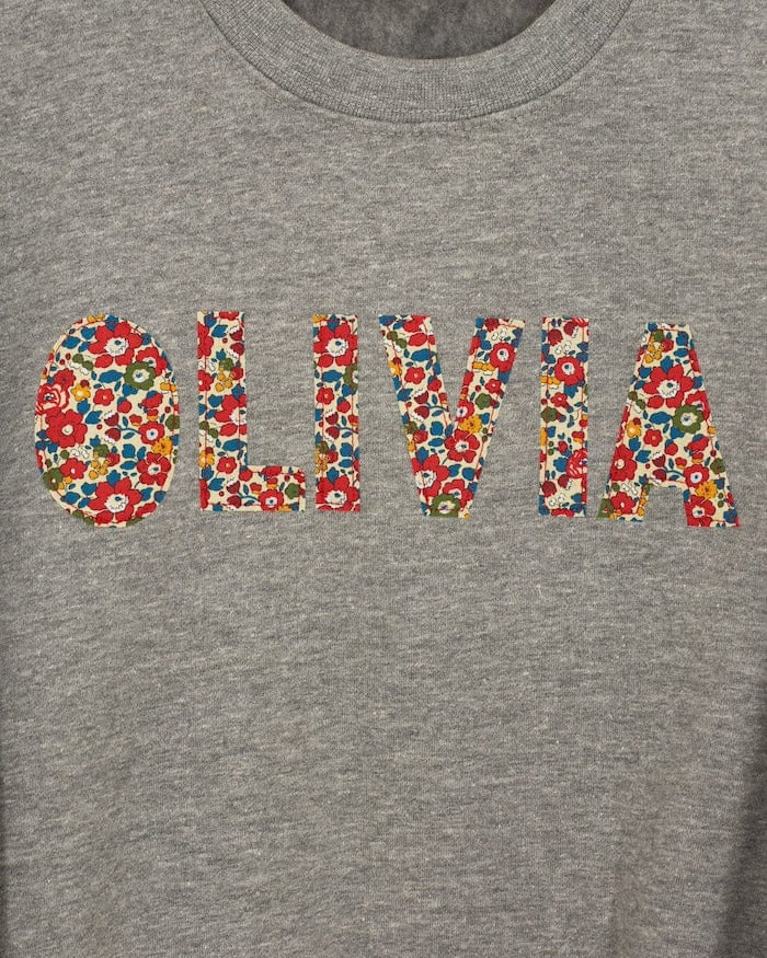 a grey kids personalised sweatshirt with the name Olivia on it cut from Betsy Ann Liberty print.