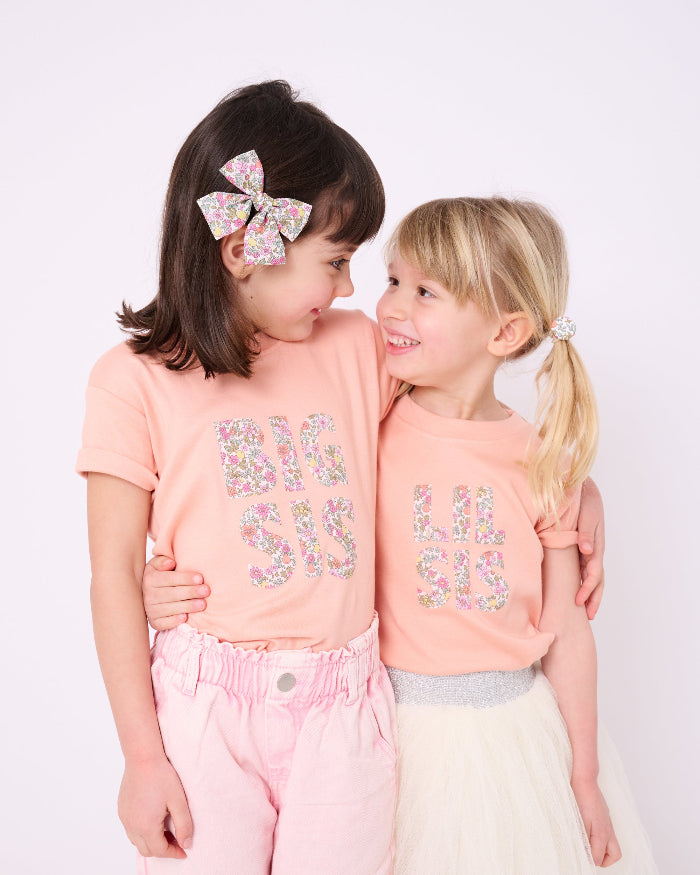 A girl wearing a BIG SIS pale Pink T-Shirt in Choice of Liberty Print as a proud big sister and a little sister wearing a 'lil sis' tee