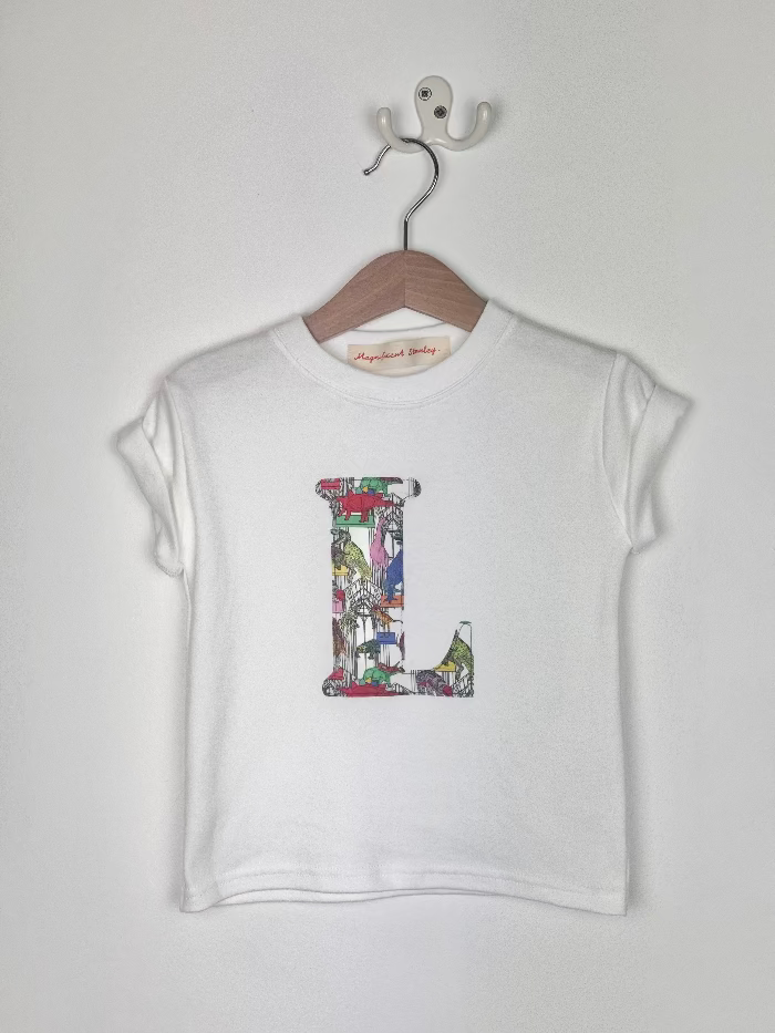 White t-shirt with colorful dinosaur Liberty print 'L' design on a hanger against a white background