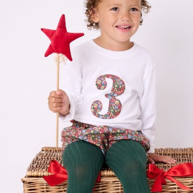a little girl wearing a white birthday t-shirt with a number 3 cut from liberty floral print on the front