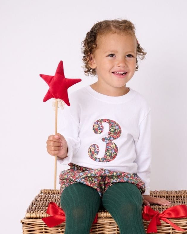 a little girl wearing a white birthday t-shirt with a number 3 cut from liberty floral print on the front