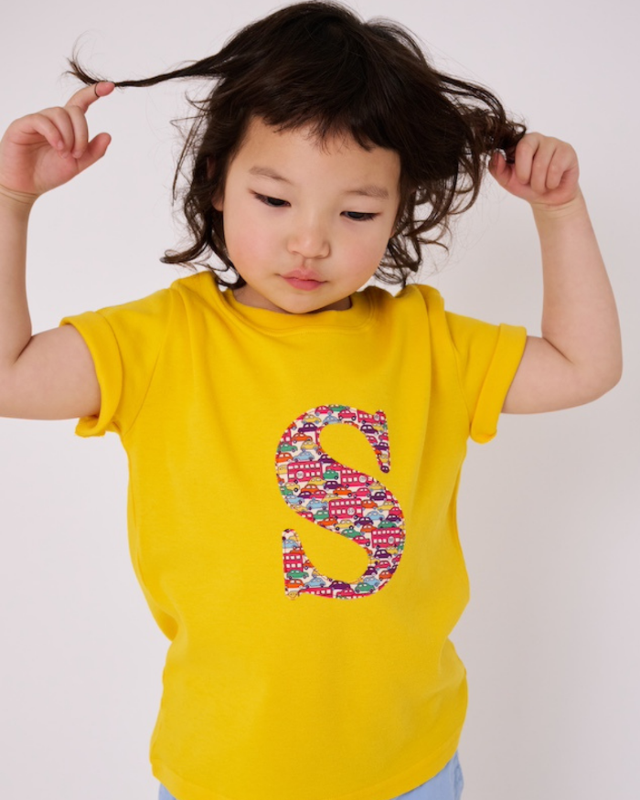 a smiling 3 year old boy wearing a yellow personalised t-shirt with his initial cut from cars liberty print on the front.