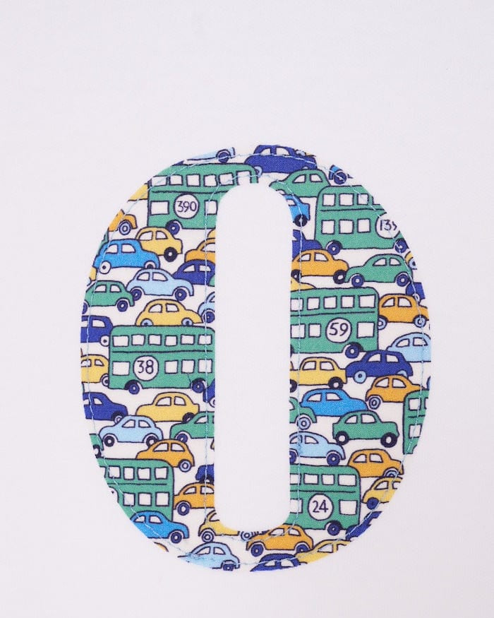 a close up of a personalised cotton baby romper with his initial on the front in hop on hop off liberty print featuring cars and London buses.