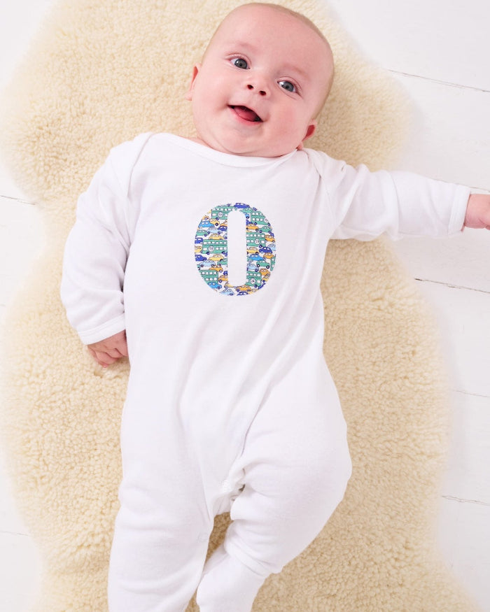 a happy baby wearing a personalised cotton baby romper with his initial on the front in hop on hop off liberty print featuring cars and London buses.