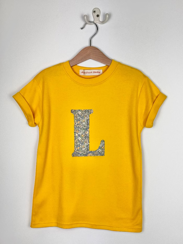 Yellow t-shirt with dragon liberty print letter 'L' on a hanger against a white background