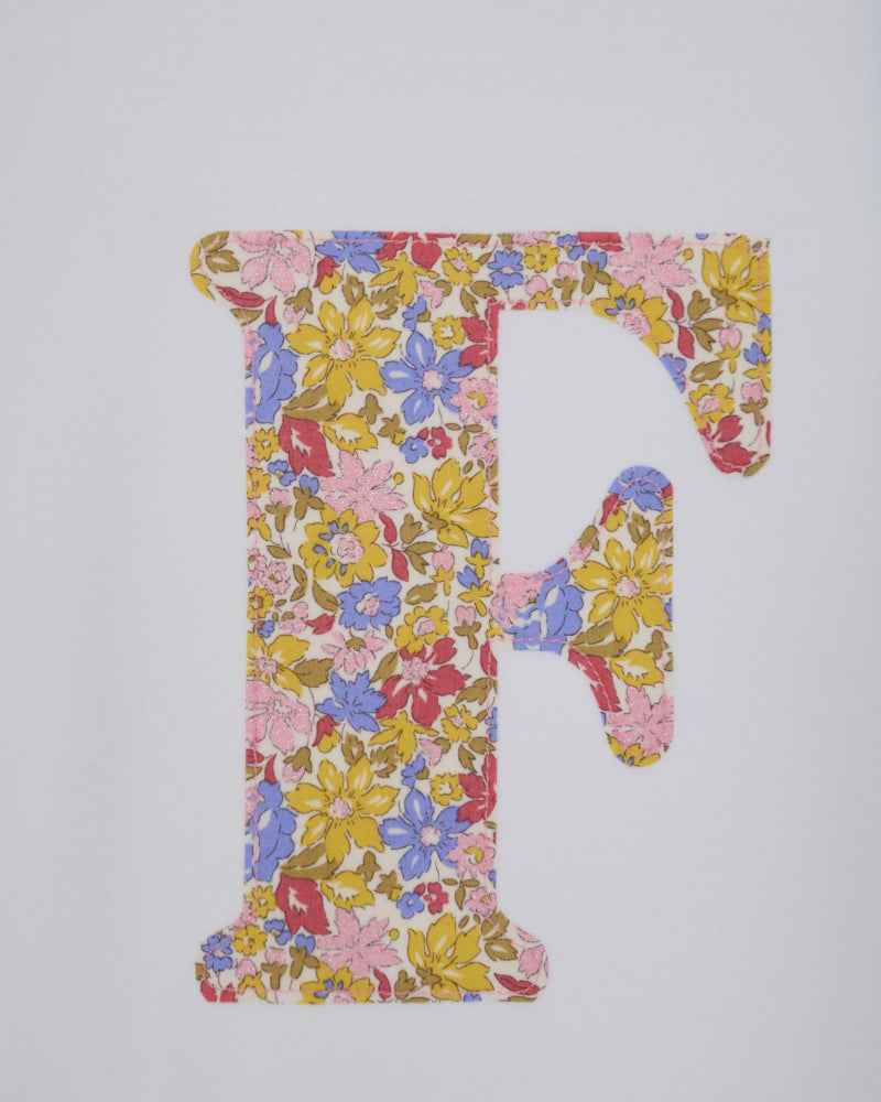 A decorative capital letter F filled with a dense floral Liberty print in pink, yellow, blue, and red tones.