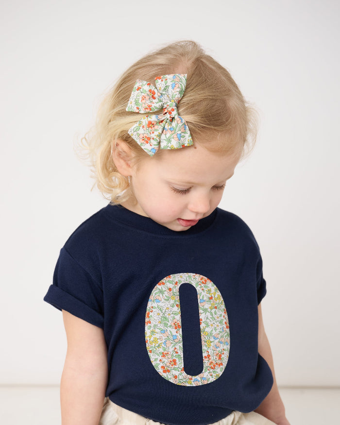 Child wearing a navy blue shirt with a floral number '0' on a white background
