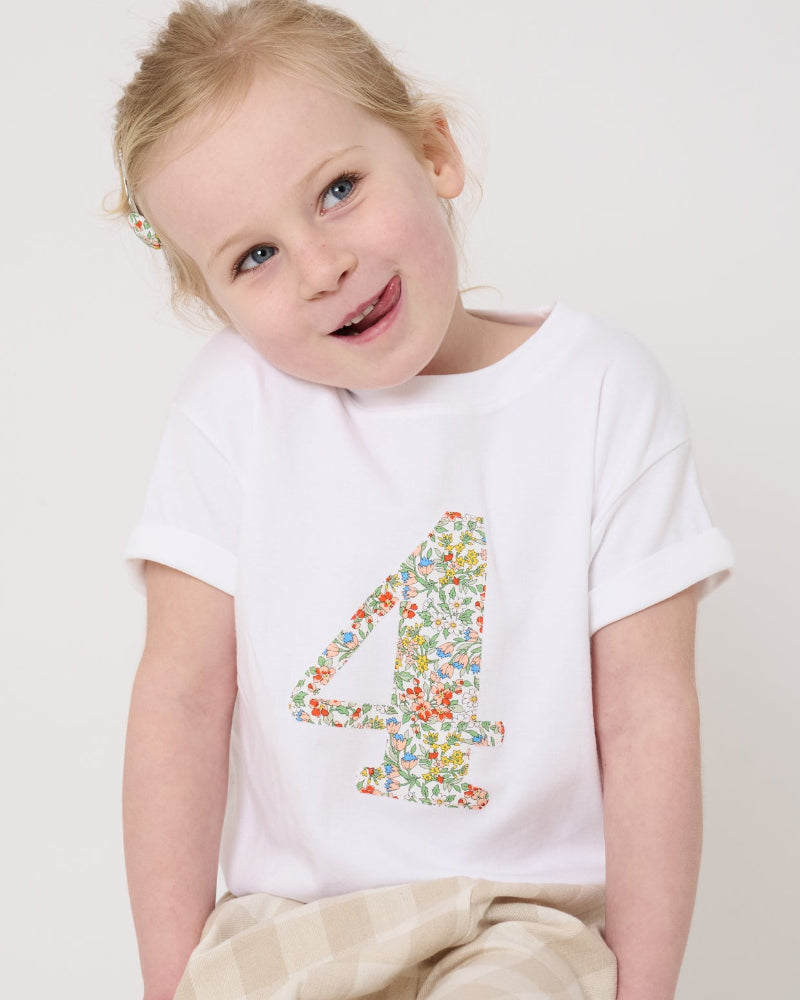 A 4 year old girl wearing a white cotton birthday t-shirt with the number 4 sewn on the front cut from liberty Nazanin fabric.