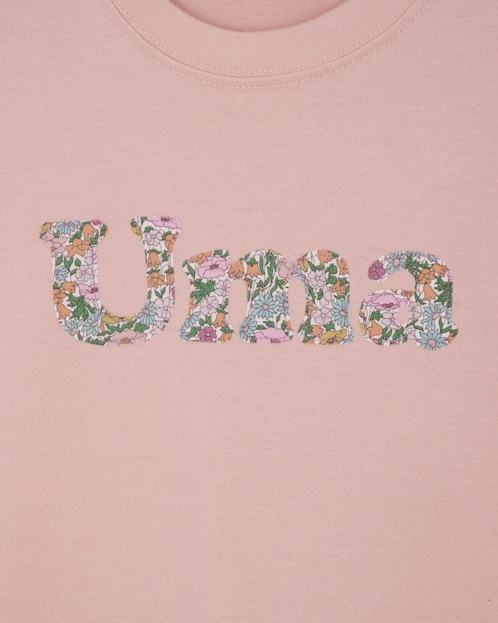A soft pink kids t-shirt with a name cut from Liberty print in lowercase letters.