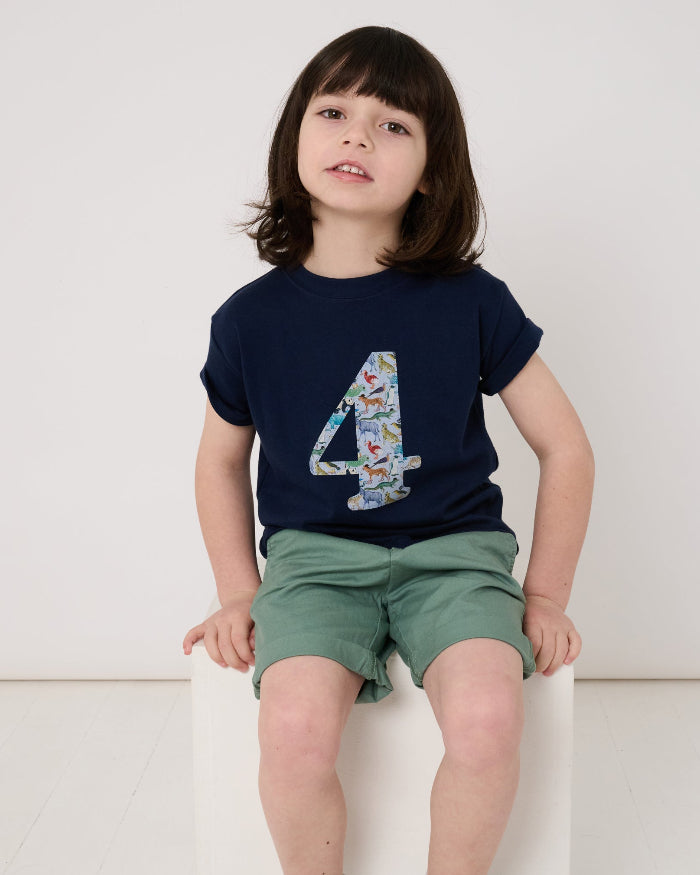 A 4 year old boy wearing a navy cotton t-shirt with the number 4 sewn on the front cut from liberty Quey 2 zoo animal print.