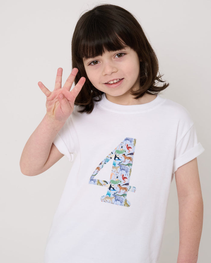 A 4 year old boy wearing a white cotton t-shirt with the number 4 sewn on the front cut from liberty Quey 2 zoo animal print.