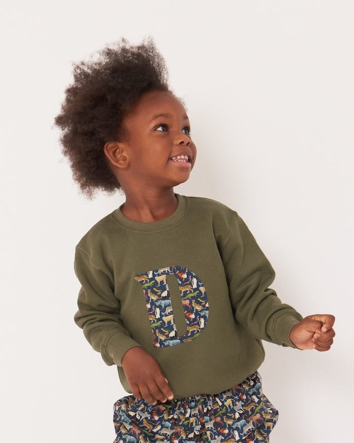 A 3 year old boy wearing a personalised  khaki sweatshirt with an initial made from quey 2 Liberty animal print fabric.