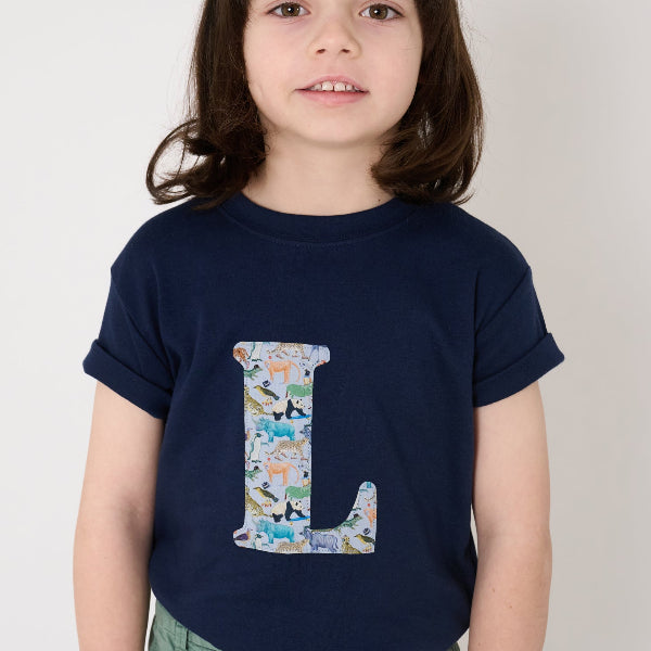 a 5 year old boy wearing a personalised kids navy t-shirt with an initial cut from Quey 2 liberty zoo animal print on the front.