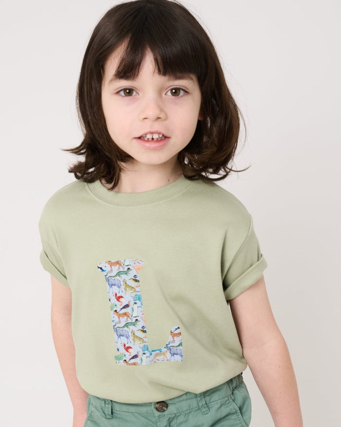 a 5 year old boy wearing a personalised kids sage green t-shirt with his initial cut from quey 2 zoo animal liberty print on the front.