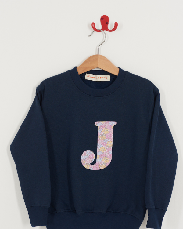 Navy blue sweatshirt with floral letter 'J' on a hanger against a white background