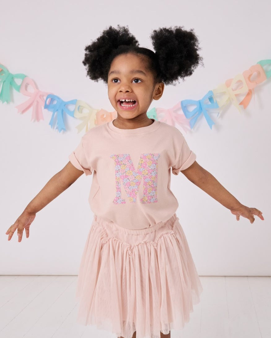 a little girl wearing a personalised kids pink t-shirt with an initial cut from sadie rose liberty floral print on the front