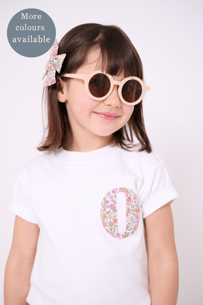 a 4 year old girl wearing a personalised white cotton kids t-shirt with a small initial on the front made from liberty print.