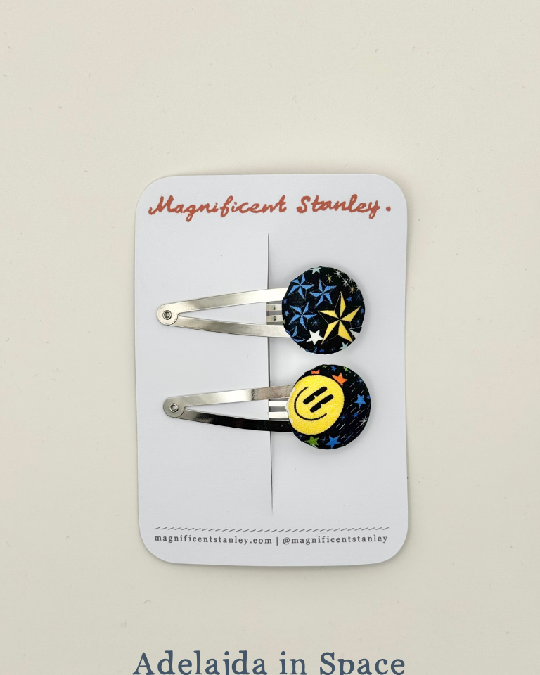 Two liberty bobble hair clips with colourful smiley face design in Adelajda in Space print on a 'Magnificent Stanley' card.