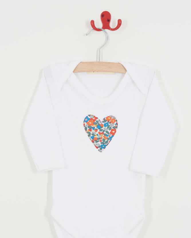 White baby onesie with a colourful heart design on a hanger against a white background