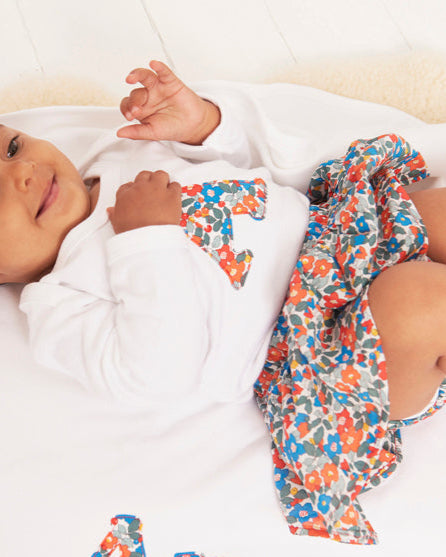 Baby lying on a white blanket with colorful liberty fabric and 'Annie' embroidered on it.