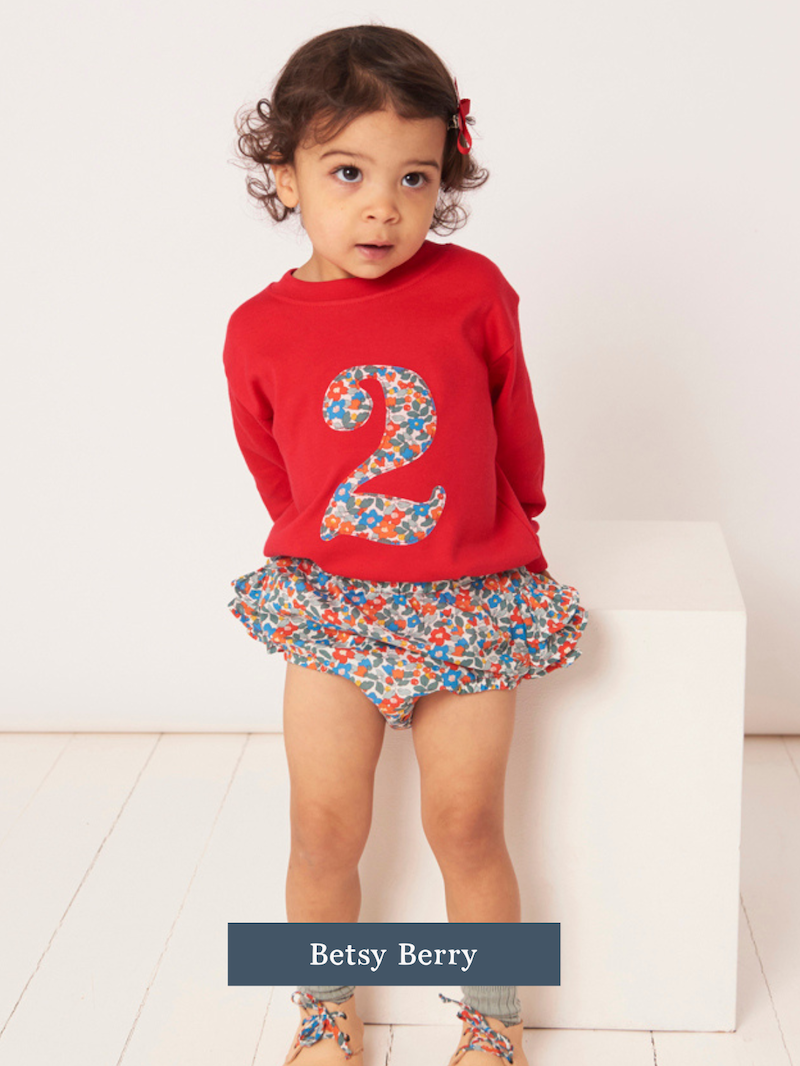 Child wearing a red t-shirt with a Liberty floral number 2 design and a matching skirt on a white background.