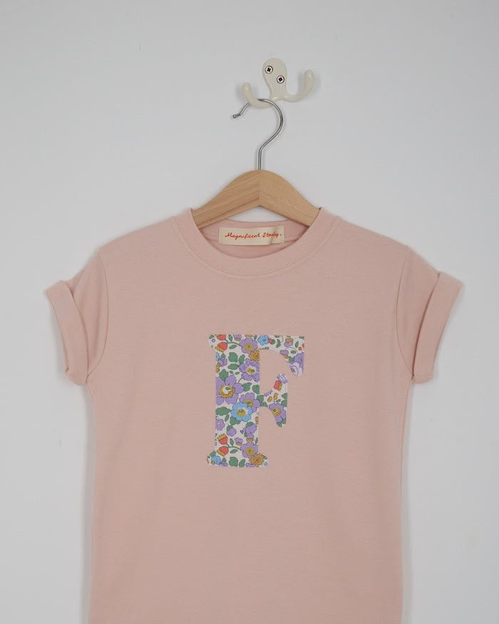 a personalised kids blush pink t-shirt with an initial cut from Betsy Purple liberty floral print on the front.