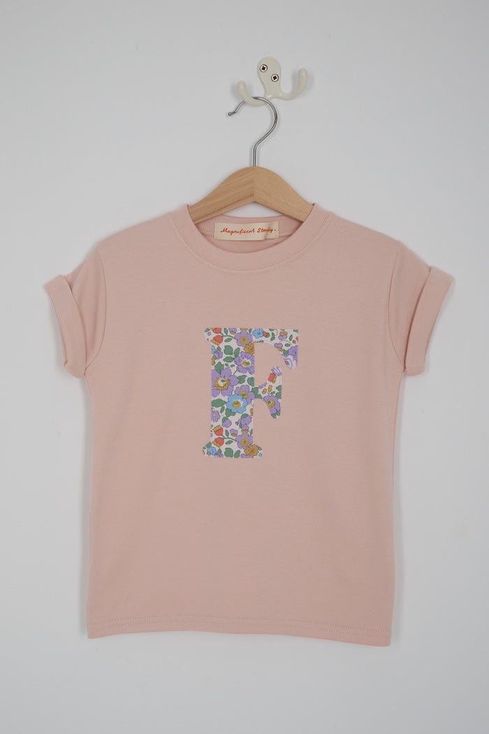 a personalised kids blush pink t-shirt with an initial cut from Betsy Purple liberty floral print on the front.
