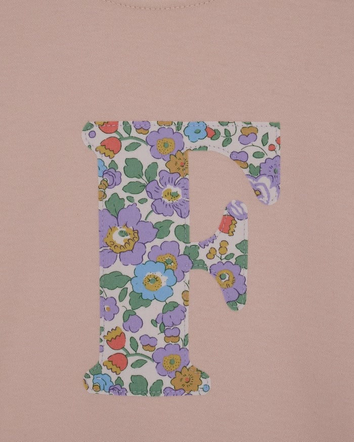 a close up of the appliqué stitching on a personalised kids blush pink t-shirt with an initial cut from Betsy Purple liberty floral print on the front.
