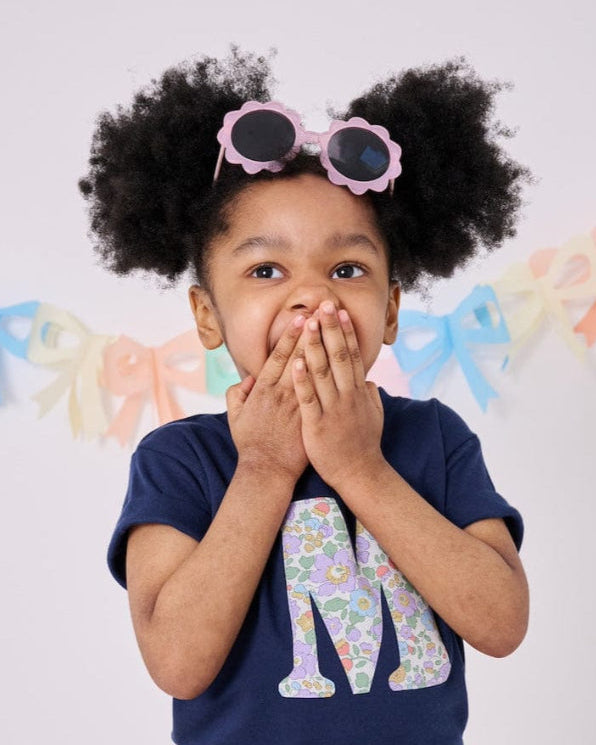 a 3 year old girl wearing a personalised kids navy t-shirt with an initial cut from betsy purple liberty floral print on the front