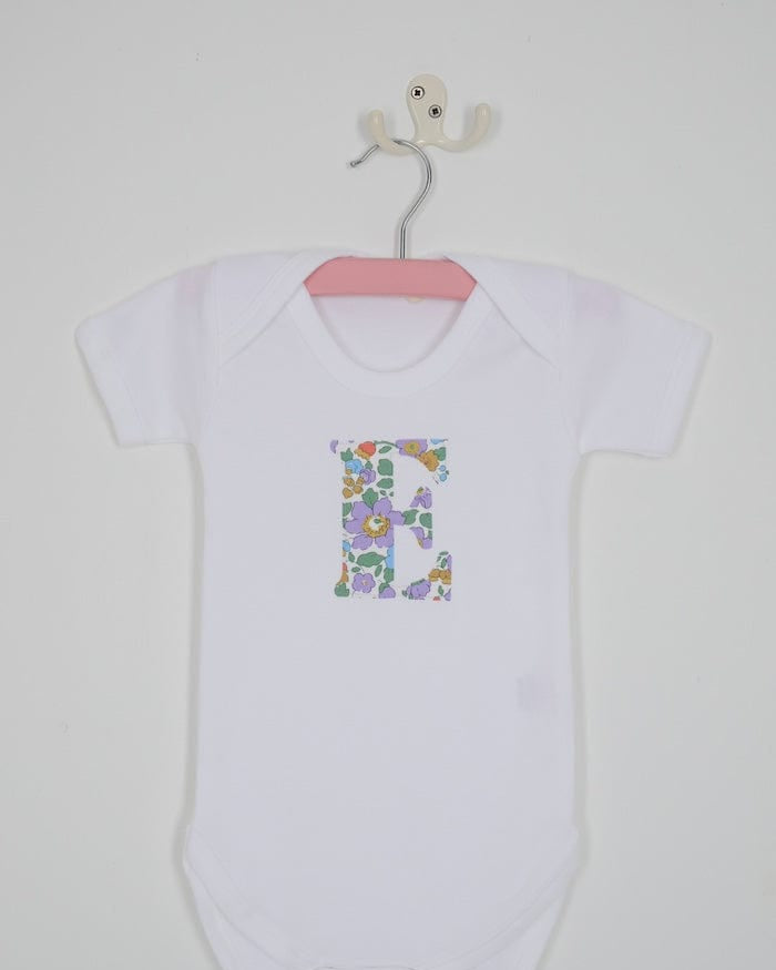 a personalised bodysuit baby grow with an initial cut from floral betsy purple Liberty print