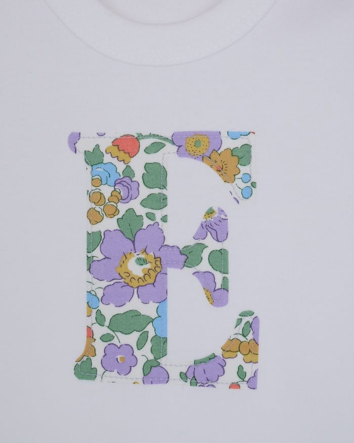 a personalised bodysuit baby grow with an initial cut from floral betsy purple Liberty print, a close up of the appliqué stitching