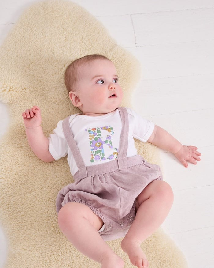 a 6 month old baby wearing a personalised bodysuit baby grow with her initial cut from floral betsy purple Liberty print