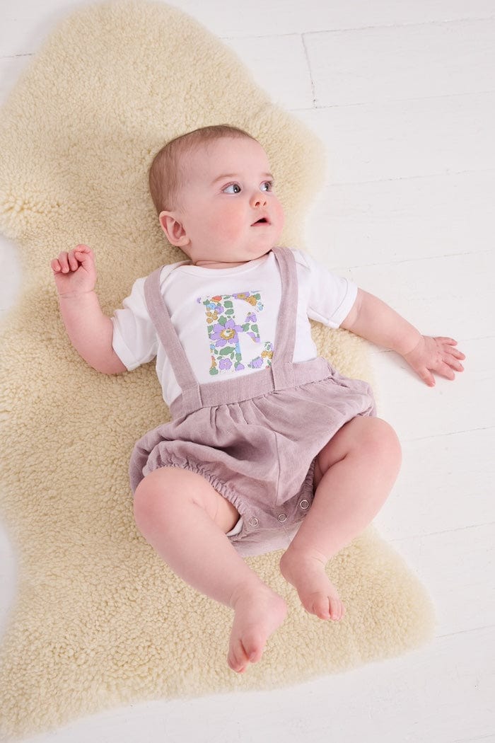 a 6 month old baby wearing a personalised bodysuit baby grow with her initial cut from floral betsy purple Liberty print