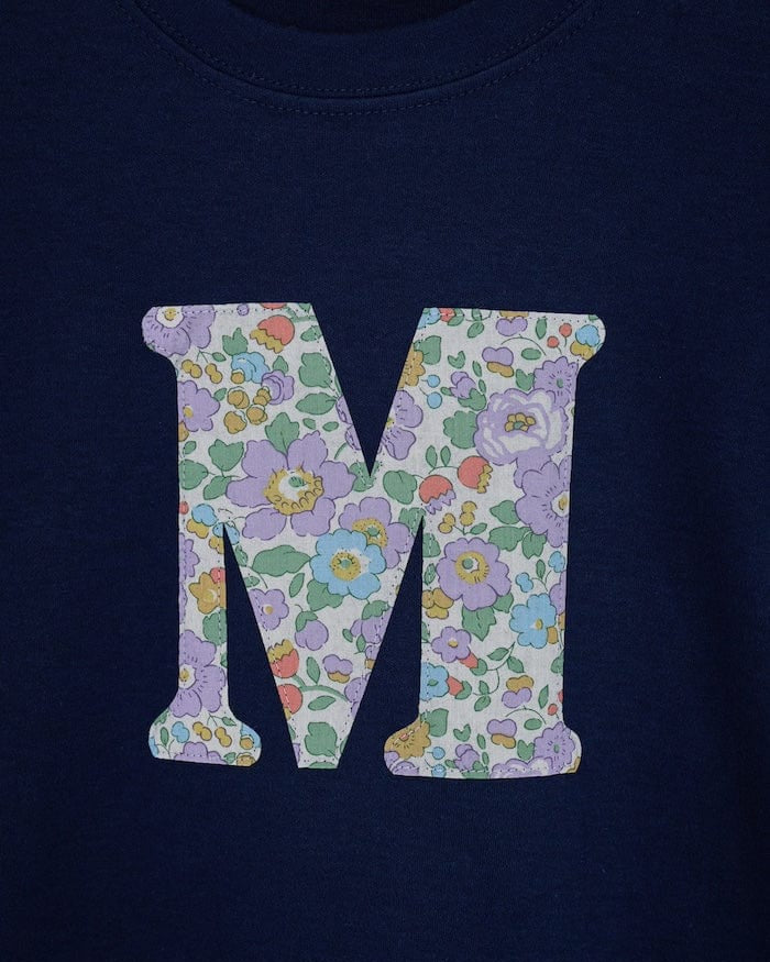 a personalised kids navy t-shirt with an initial cut from betsy purple liberty floral print on the front. Close up on the stitching.