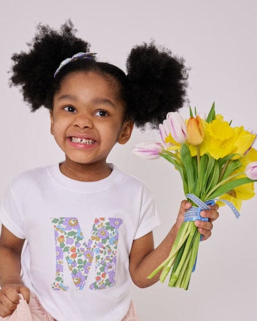 a 4 year old girl wearing a personalised kids white t-shirt with an initial cut from betsy purple liberty floral print on the front