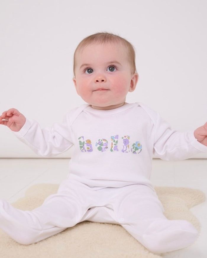 A 6 month old baby girl wearing a white cotton baby romper with the word hello made from Betsy Liberty Print sewn onto the front.