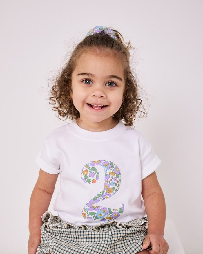 a 2 year old girl wearing a white birthday t-shirt with a number 2 cut from betsy purple liberty floral print on the front