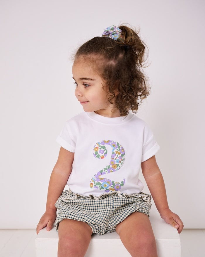 a 2 year old girl wearing a white birthday t-shirt with a number 2 cut from betsy purple liberty floral print on the front