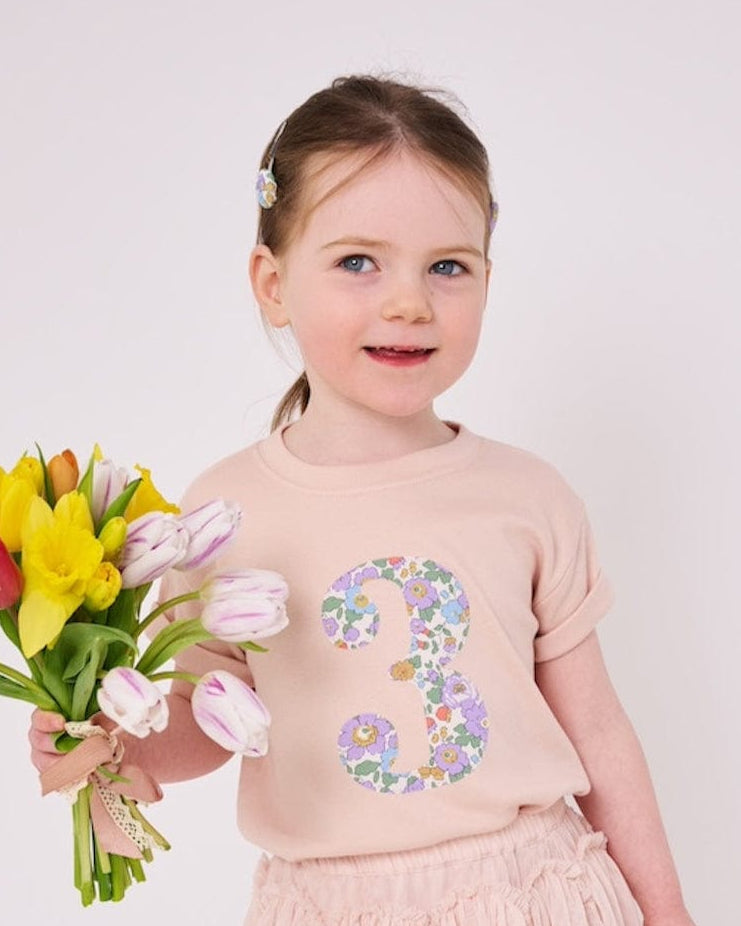 a 3 year old girl wearing a pink birthday t-shirt with a number 3 cut from betsy purple liberty floral print on the front