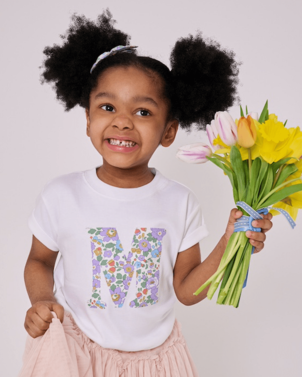 A 3 year old girl wearing a personalised white cotton t-shirt with her initial on in Betsy Purple floral Liberty fabric.
