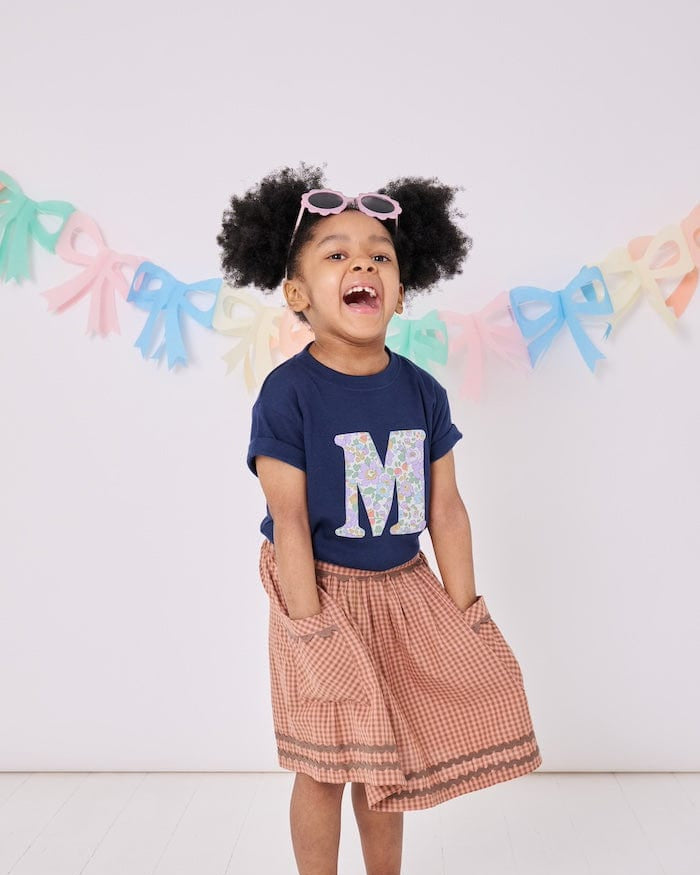 a 3 year old girl wearing a personalised kids navy t-shirt with an initial cut from betsy purple liberty floral print on the front