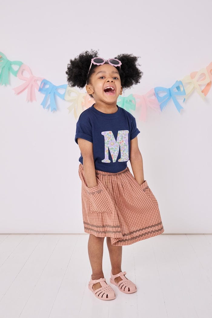 a 3 year old girl wearing a personalised kids navy t-shirt with an initial cut from betsy purple liberty floral print on the front