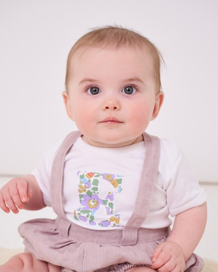 a 6 month old baby wearing a personalised bodysuit baby grow with her initial cut from floral betsy purple Liberty print