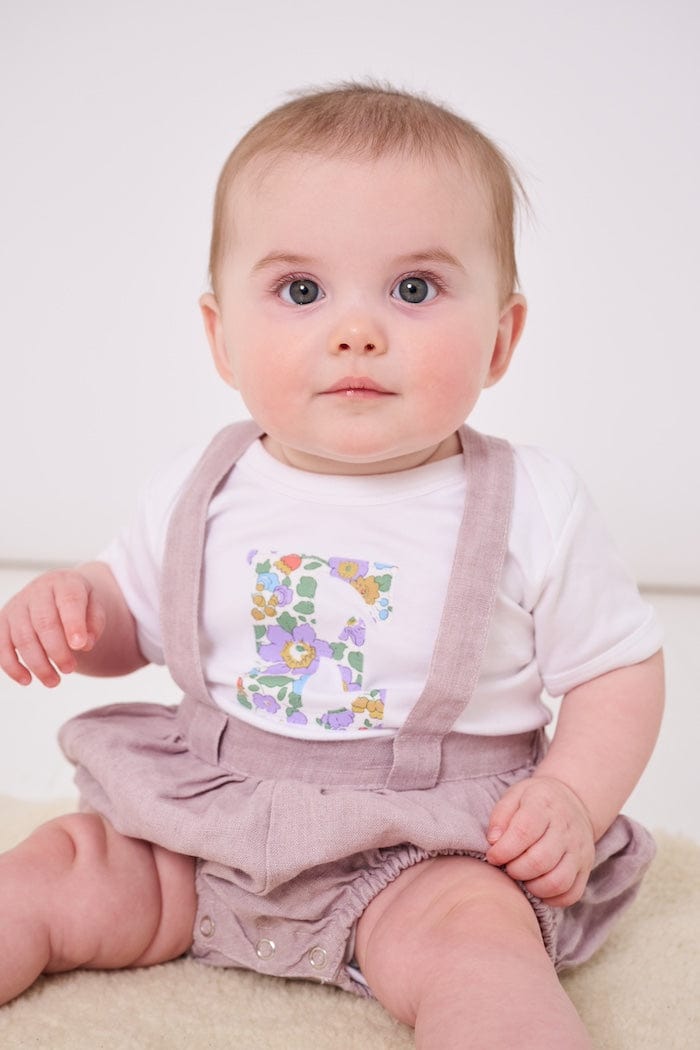 a 6 month old baby wearing a personalised bodysuit baby grow with her initial cut from floral betsy purple Liberty print