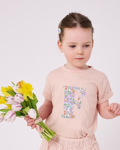 a little girl wearing a personalised kids blush pink t-shirt with an initial cut from Betsy Purple liberty floral print on the front.