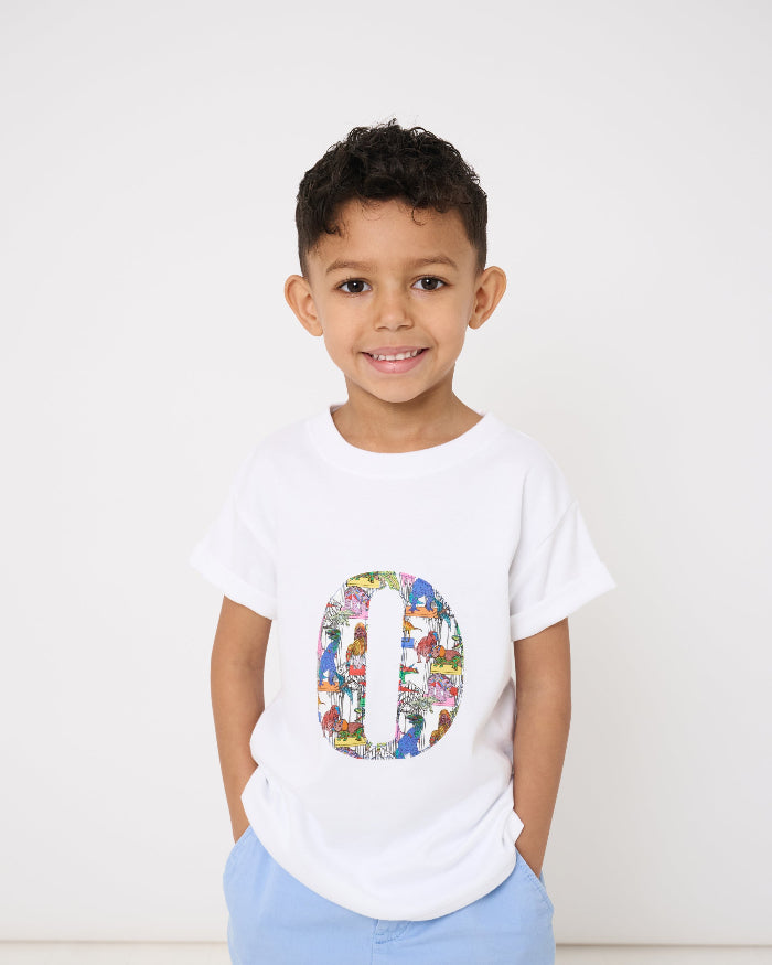 A smiling 4 year old wearing a white kids T-Shirt with his initial on the front in Dinosaur Liberty Print