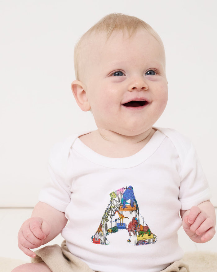 A baby wearing a personalised baby bodysuit with his initial cut from dinosaur liberty print on the front